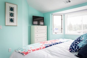 A bedroom with a bed, a dresser, a television on top of the dresser, and a window with a view of trees. - Oasis 321 | Beachfront Condo | Downtown + Tart Trail (Traverse City)