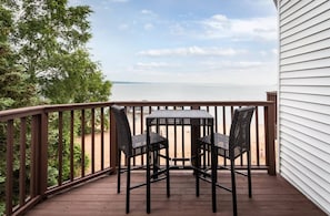 A wooden deck with a table and two chairs, overlooking a body of water. - Oasis 321 | Beachfront Condo | Downtown + Tart Trail (Traverse City)