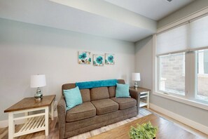 A living room with a brown sofa, two side tables, and a window with blinds.