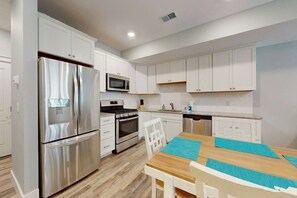 A modern kitchen with white cabinetry, stainless steel appliances, a wooden dining table with blue placemats, and a white chair.
