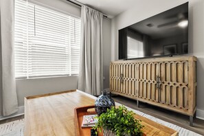A modern living room with a wooden coffee table, a potted plant, a magazine, and a television on a wooden cabinet. - Tuscaloosa Retreat ~ Minutes to Bryant-Denny (Tuscaloosa)