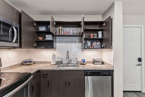 A modern kitchen with dark wood cabinets, a stainless steel dishwasher, and a microwave. - Tuscaloosa Retreat ~ Minutes to Bryant-Denny (Tuscaloosa)