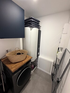 A laundry area with a washing machine, stacked pillows, and a basket on a wooden counter. - THE VILLA IN THE HEART OF BUCH, 300 meters from the market, 3 km from Arcachon, and 7 km from the Dune du Pilat (La Teste-de-Buch)