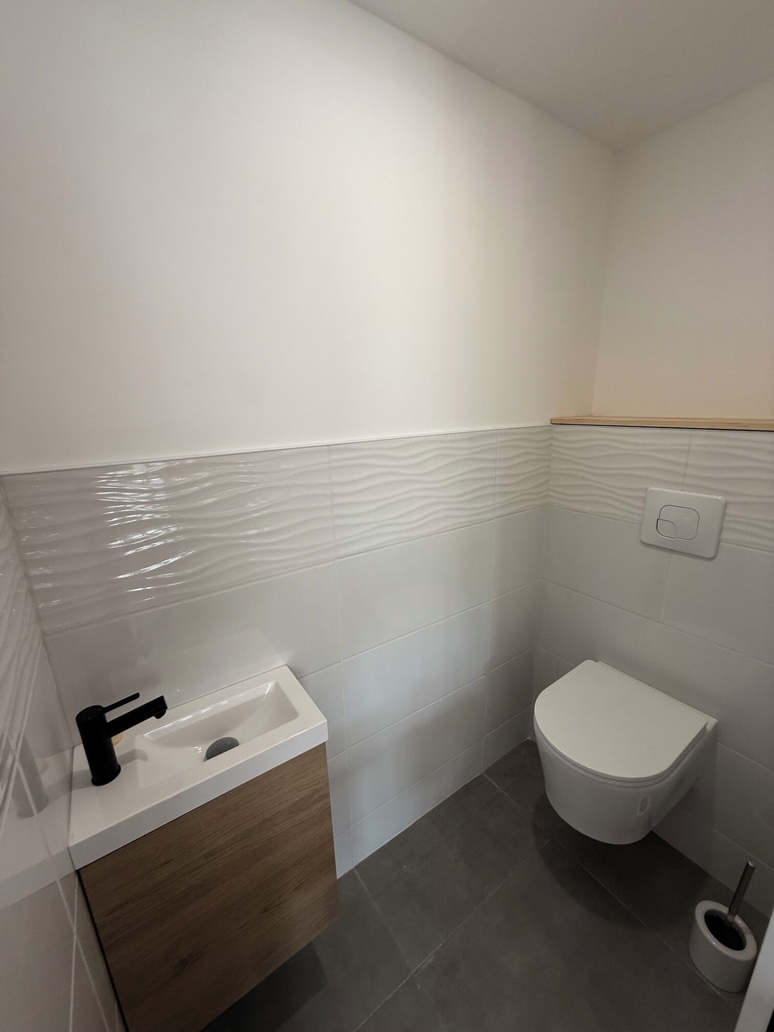 A small bathroom with a white sink, a toilet, and a wooden vanity.