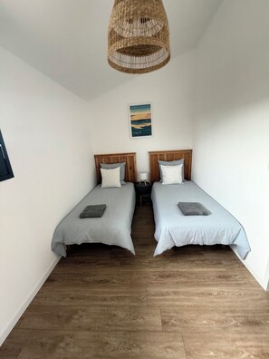 A room with two beds, wooden flooring, a hanging light fixture, and a wall-mounted picture. - THE VILLA IN THE HEART OF BUCH, 300 meters from the market, 3 km from Arcachon, and 7 km from the Dune du Pilat (La Teste-de-Buch)