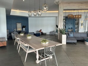 Ein modernes Wohnzimmer mit Essbereich, ausgestattet mit einem langen Holztisch, grauen Sofas und hängenden, kugelförmigen Leuchten.