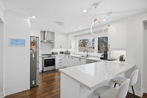 A modern kitchen with white cabinetry, stainless steel appliances, and a large island with seating. - Upscale 5BR Home + 2 Offices + Kids Playroom + Ideal for large families (Mississauga)