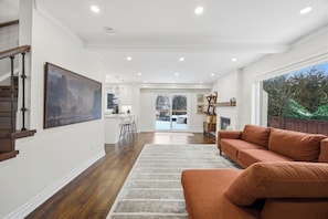 A spacious living area with a large painting, a wooden staircase, and a view through a glass door to an outdoor area. - Upscale 5BR Home + 2 Offices + Kids Playroom + Ideal for large families (Mississauga)