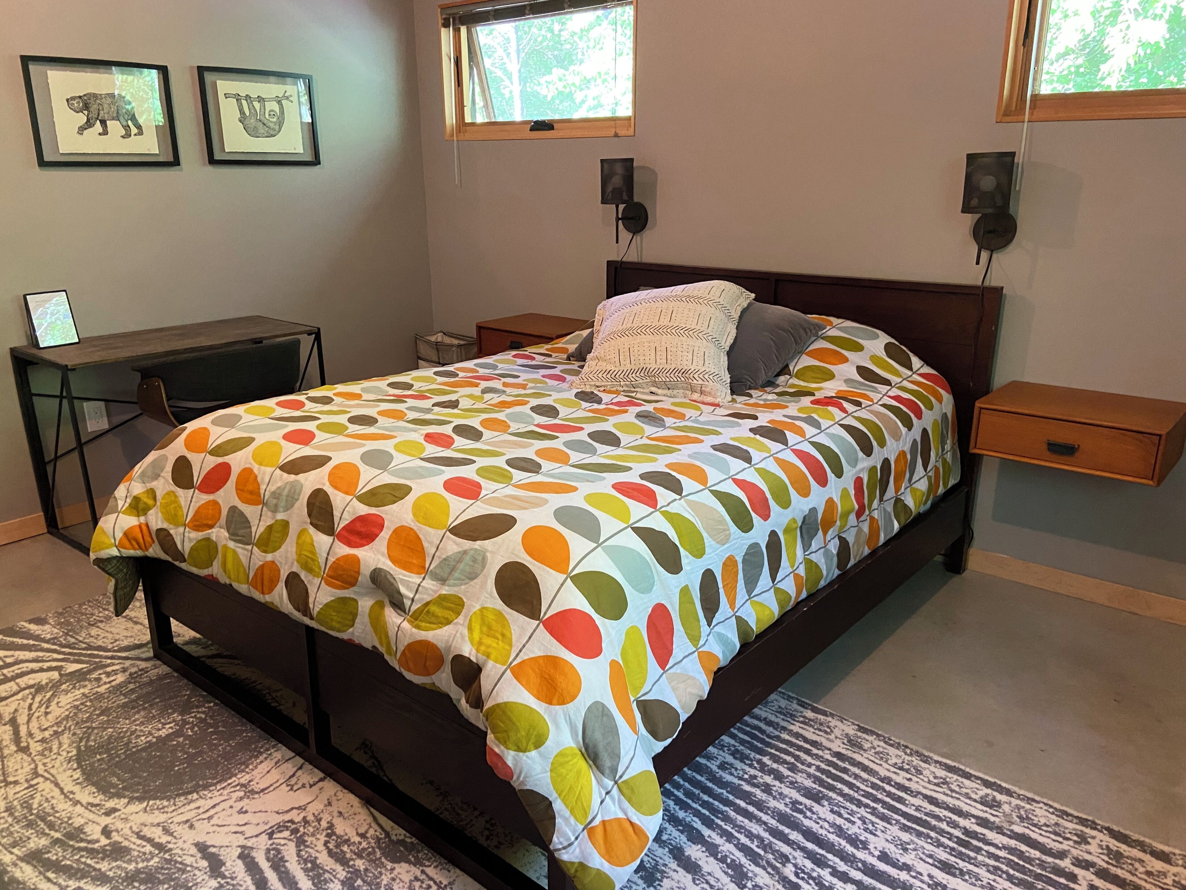 A bedroom with a bed, bedside tables, a desk, and framed pictures on the wall.