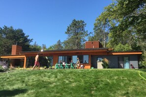 A modern house with a flat roof, large windows, and a covered outdoor area with chairs. - Stunning 6-bedroom modern lake house perfect for families (Erhard)