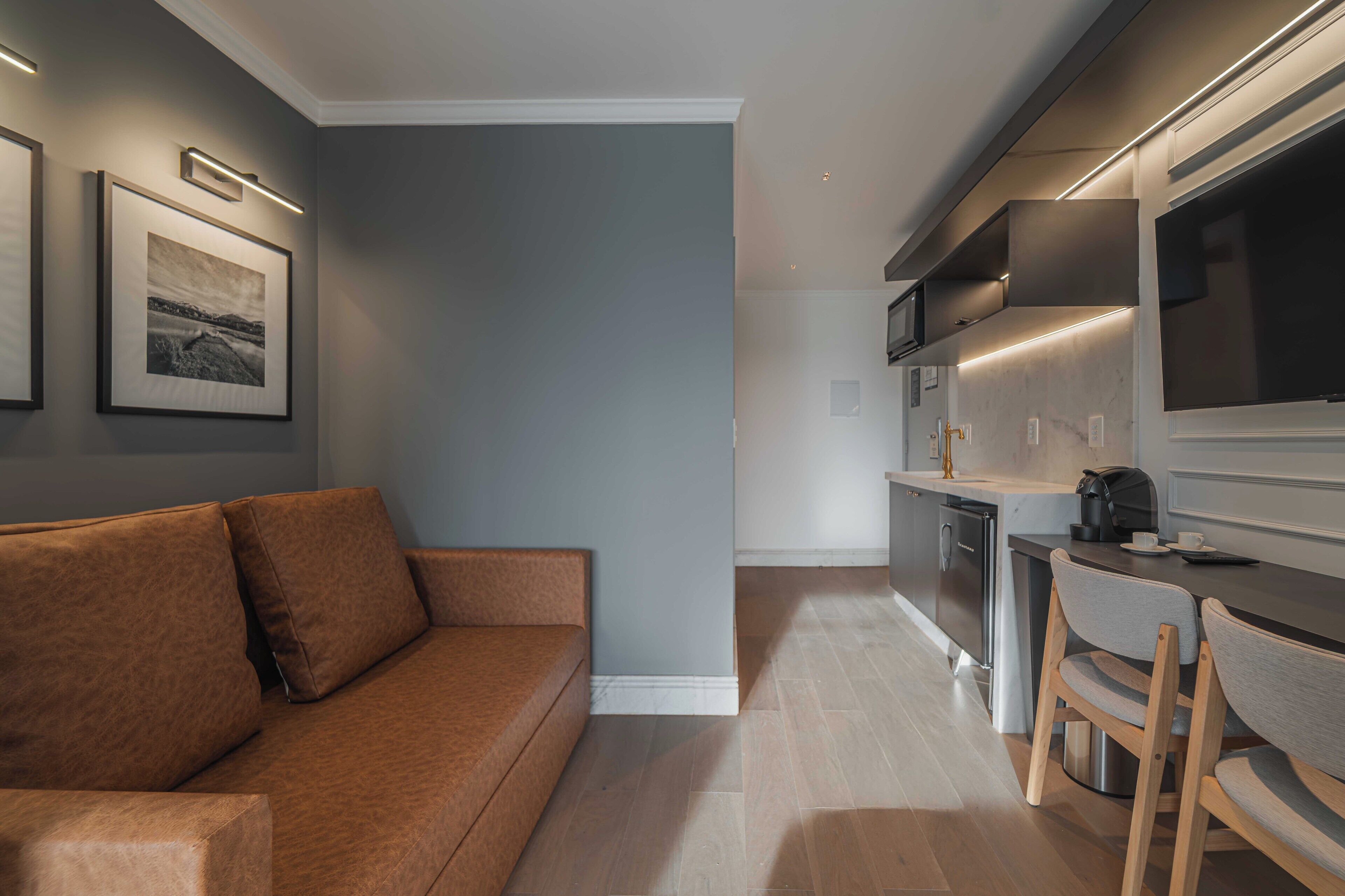 A modern living room with a brown sofa, a kitchen with a built-in oven and microwave, and a dining area with a table and chairs.