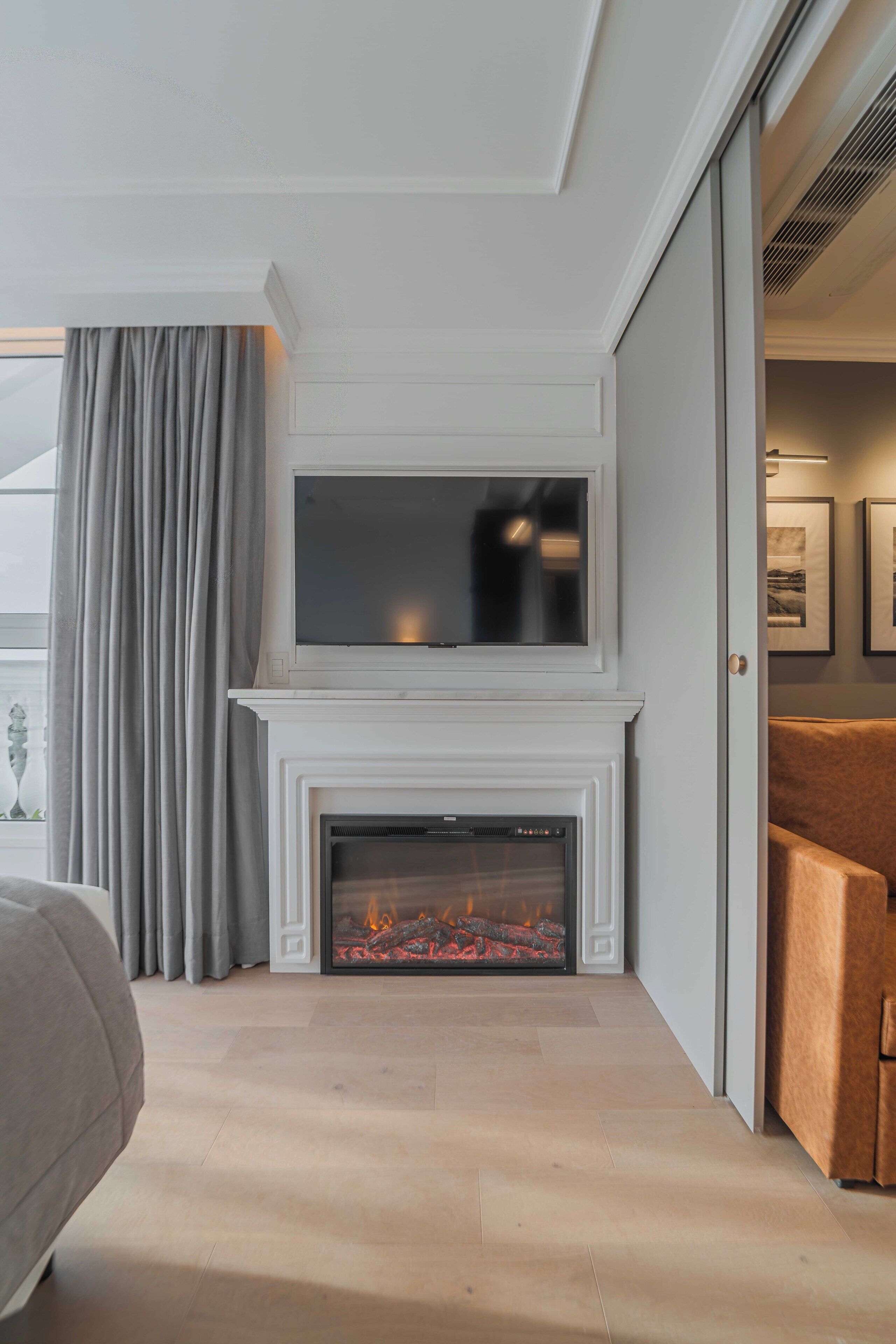 Una sala de estar moderna con chimenea, un televisor de pantalla plana montado encima y un ventanal con cortinas.