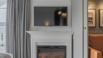 Una sala de estar moderna con chimenea, un televisor de pantalla plana montado encima y un ventanal con cortinas.