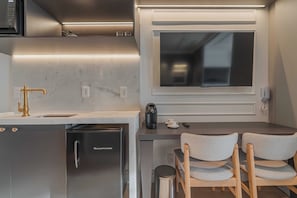 A compact kitchenette with a built-in microwave, a stainless steel dishwasher, and a coffee maker. There is a small table with two chairs and a window above it.
