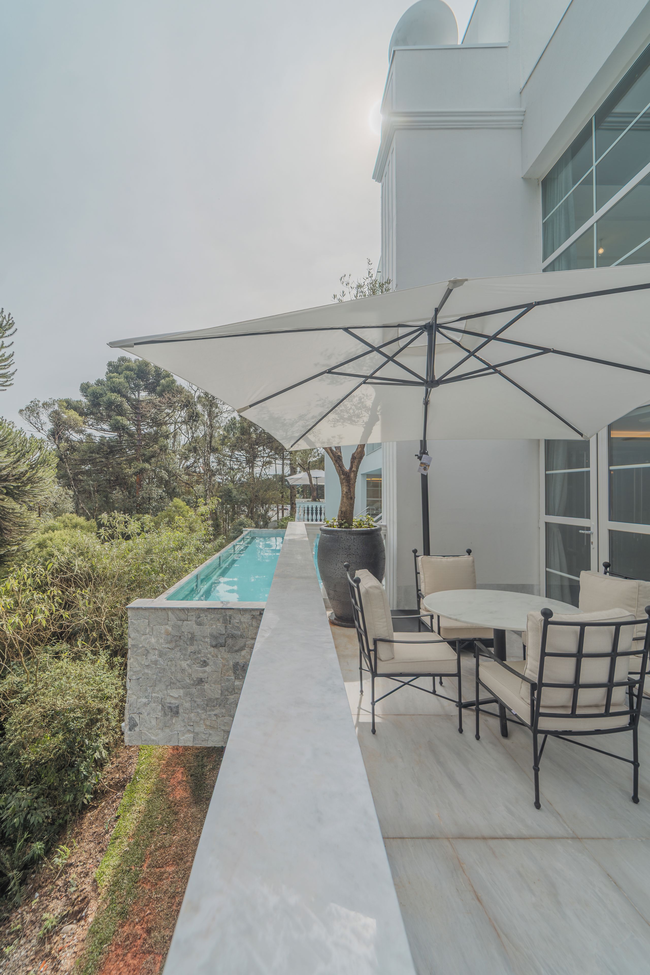 A modern outdoor patio with a pool, seating area, and a large umbrella providing shade.
