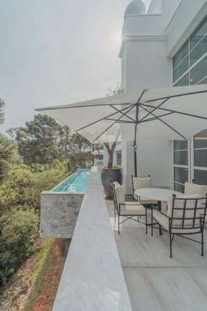 A modern outdoor patio with a pool, seating area, and a large umbrella providing shade.