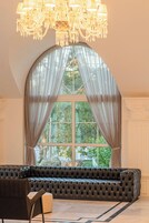 Un'ampia sala con una grande finestra ad arco, un'elegante poltrona in pelle scura e un lampadario decorato.