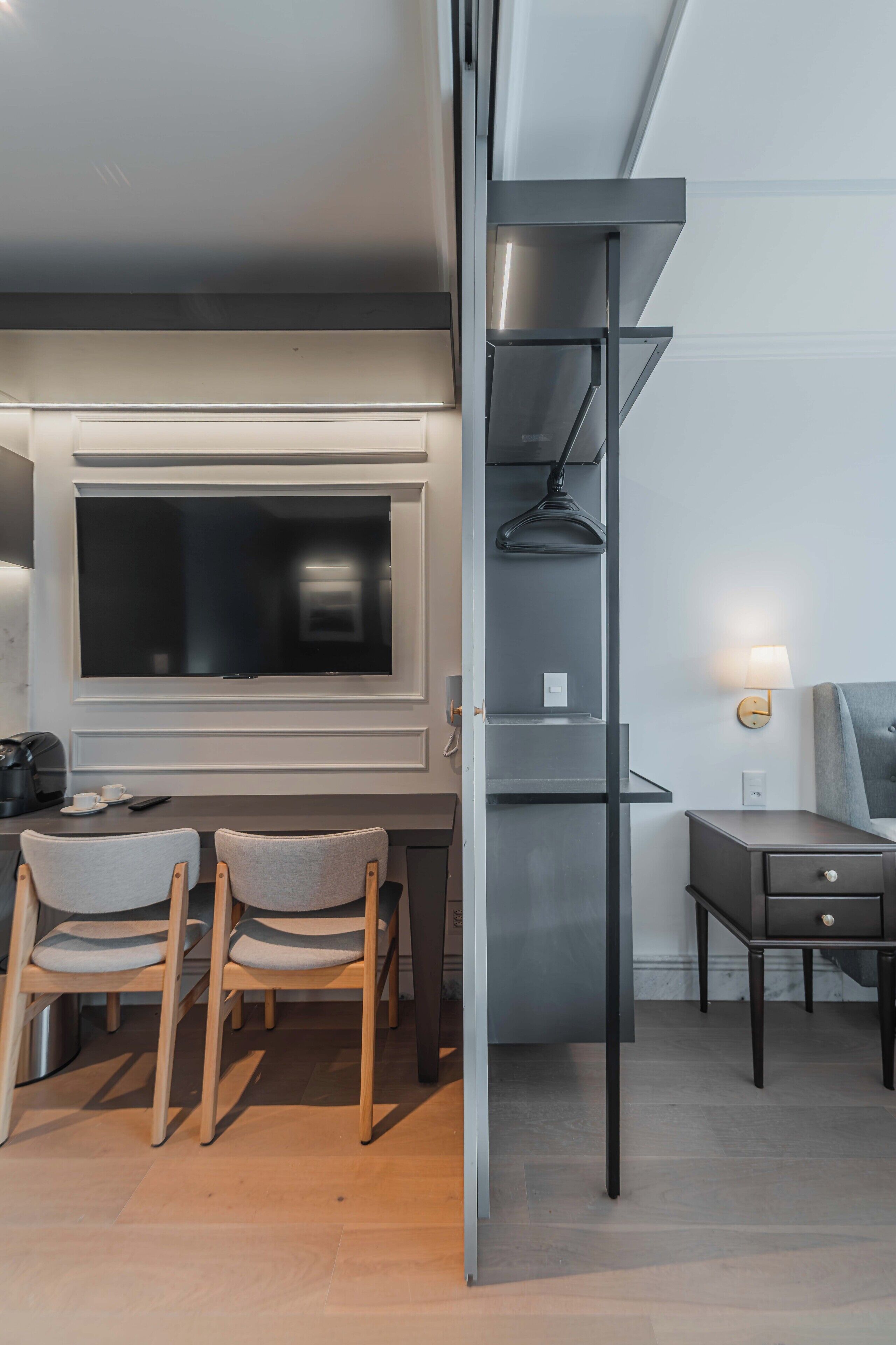 A modern room with a flat-screen TV, a desk, two chairs, and a small table with a coffee maker.