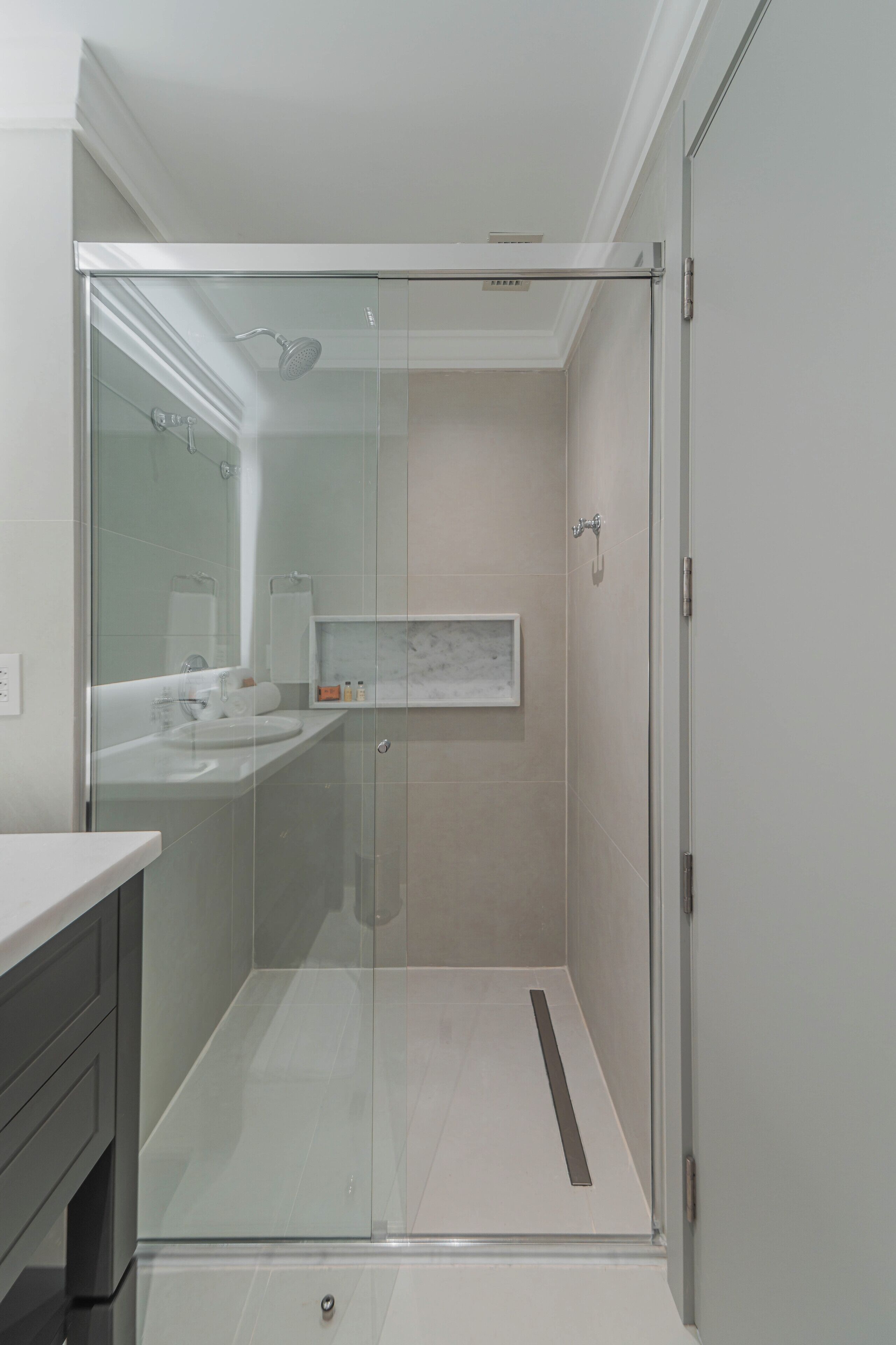Un baño moderno con ducha envuelta en cristal, lavamanos blanco y tocador con encimera de mármol.
