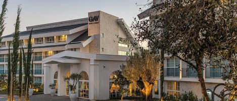 A modern hotel with a prominent 'GAV' sign, a landscaped entrance, and a mix of architectural styles.