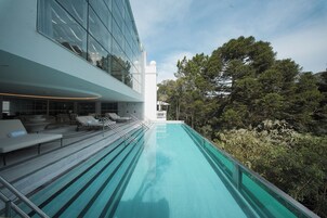 Un edificio moderno con fachada de vidrio, piscina en la azotea y mobiliario exterior.