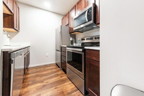 A kitchen with stainless steel appliances, wooden cabinets, and a white countertop. - Landing | Spectacular 1BD, Gym, Yoga Studio (Omaha)