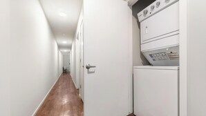 A laundry room with a washing machine and dryer, a wooden floor, and white walls. - Landing | Stunning 1BD, Gym, Yoga Studio (Omaha)
