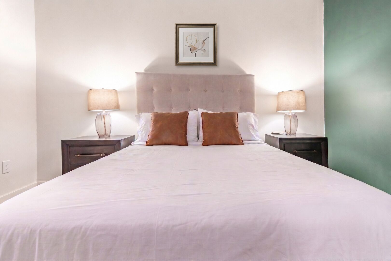 A hotel room with a large bed, two bedside tables, and a framed picture on the wall.
