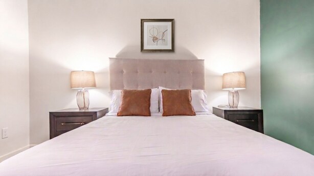 A hotel room with a large bed, two bedside tables, and a framed picture on the wall. - Landing | Stunning 1BD, Gym, Yoga Studio (Omaha)