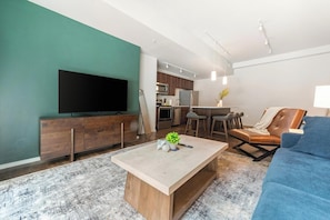 Ein modernes Wohnzimmer mit Flachbildfernseher, Holzmöbeln, einem Couchtisch und einem blauen Sofa.