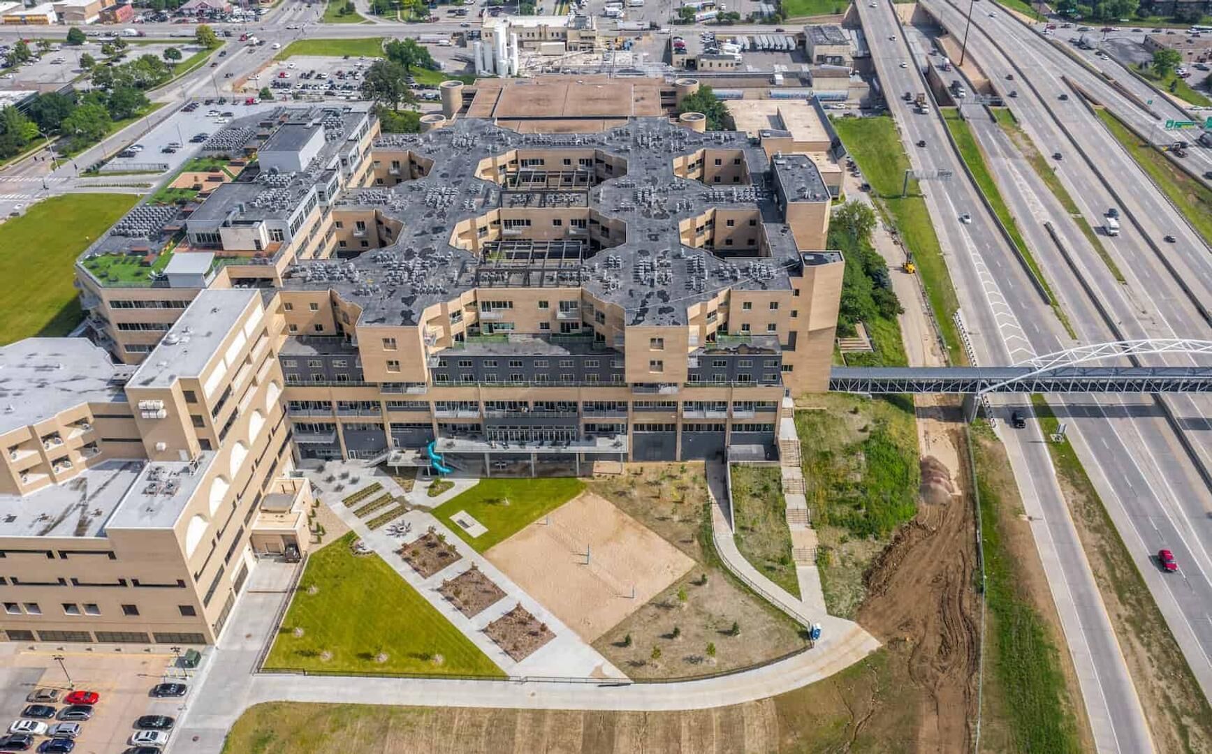 A multi-story building with a flat roof, surrounded by parking areas and a highway.