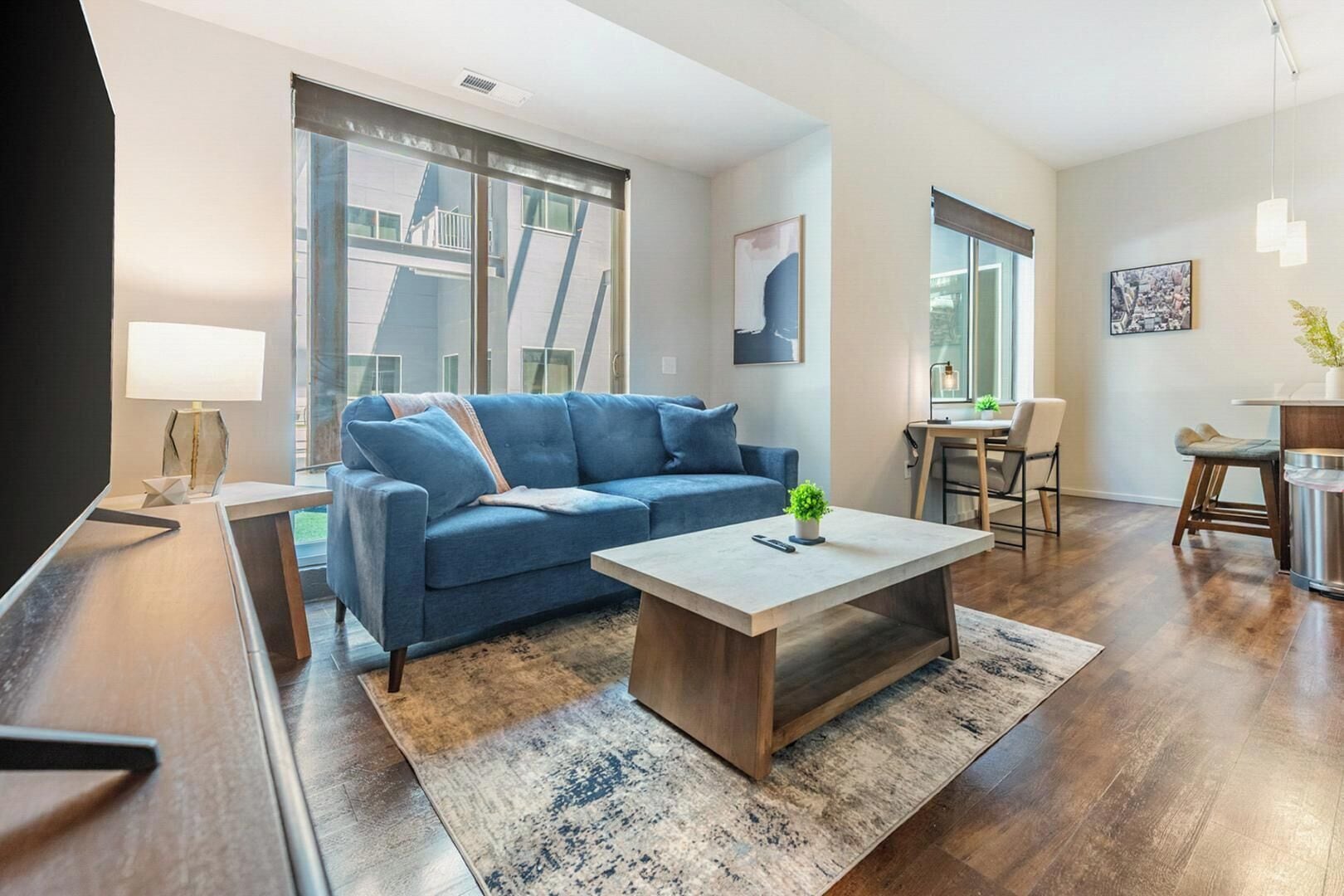 A modern living room with a blue sofa, a coffee table, and a dining area with chairs and a table.