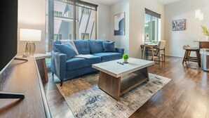 Uma sala de estar moderna com um sofá azul, uma mesa de centro e um espaço de jantar com cadeiras e uma mesa.