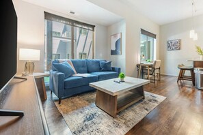 Ein modernes Wohnzimmer mit einem blauen Sofa, einem Couchtisch und einem Essbereich mit Stühlen und einem Tisch.