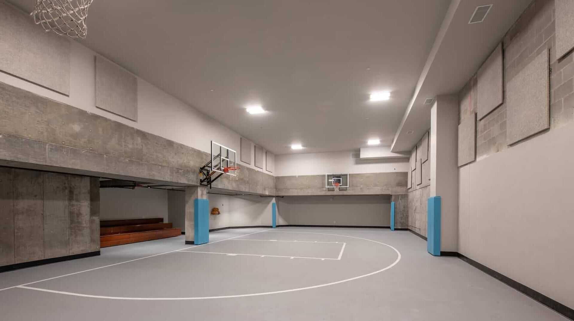 An indoor basketball court with a basketball hoop, blue pillars, and a concrete floor.