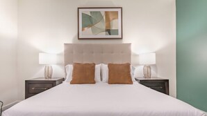 Quarto de hotel com uma cama grande, duas mesas de cabeceira e uma obra de arte abstrata emoldurada acima da cama.