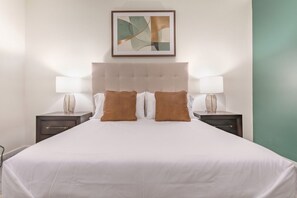 A hotel room with a large bed, two bedside tables, and a framed abstract artwork above the bed. - Landing | Modern 1BD, Yoga Studio, Gym (Omaha)