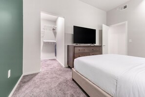 A bedroom with a bed, a dresser, a television, and a walk-in closet. - Landing | Amazing 1BD, Yoga Studio, Gym (Omaha)