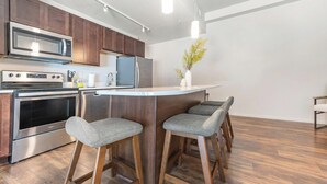 Cozinha moderna com eletrodomésticos de aço inoxidável, armários de madeira e um espaço com banquetas.