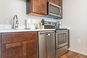 A compact kitchen with a dishwasher, oven, microwave, and a coffee maker. - Landing | Modern 1BD, Yoga Studio, Gym (Omaha)