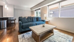 A modern living room with a sofa, a coffee table, and a window with blinds. - Landing | Stunning 1BD, Gym, Yoga Studio (Omaha)