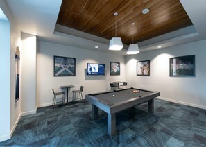 A pool table with four chairs, a television, and framed pictures on the wall. - Landing | Chic 1BD, Yoga Studio, Gym (Omaha)