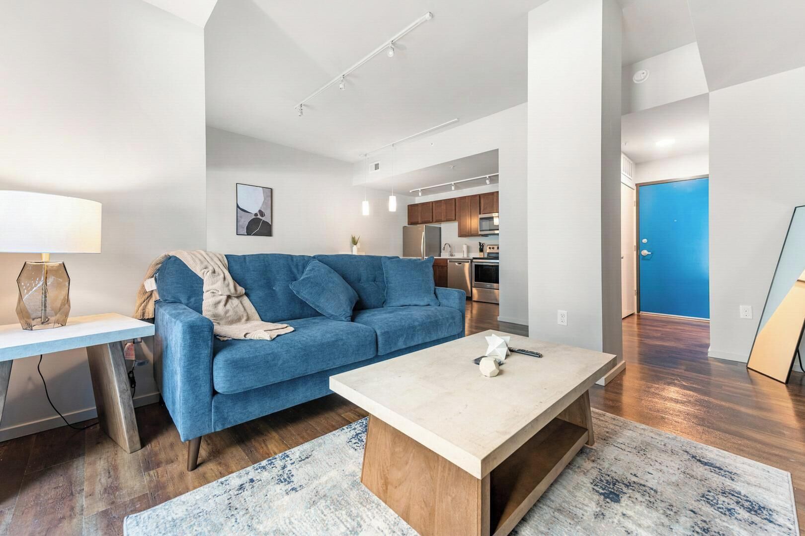 Un salon moderne avec un canapé bleu, une table basse et une cuisine en arrière-plan.