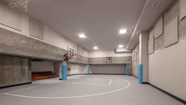Een overdekte basketbalbaan met een basketbalring, wanden met ramen en een plafond met inbouwverlichting.