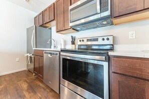 A kitchen with stainless steel appliances, wooden cabinets, and a white countertop. - Landing | Chic 1BD, Yoga Studio, Gym (Omaha)