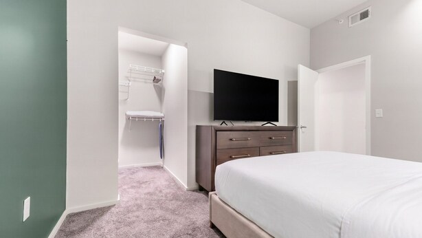 Een slaapkamer met een bed, een dressoir, een televisie en een inloopkast.