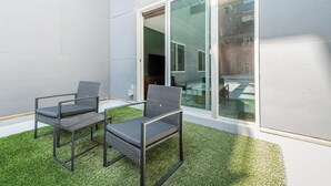 Een terras met twee stoelen en een tafel, een glazen deur naar een binnenruimte en kunstgras.