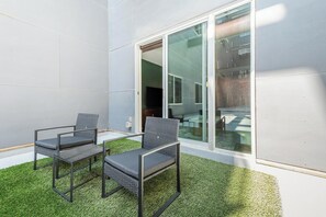A patio with two chairs and a table, a glass door leading to an indoor area, and artificial grass. - Landing | Beautiful 2BD, Yoga Studio, Gym (Omaha)
