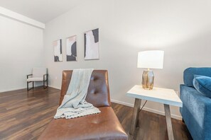 A room with a brown leather couch, a blue sofa, a small white table with a lamp, and three abstract paintings on the wall. - Landing | Beautiful 2BD, Yoga Studio, Gym (Omaha)