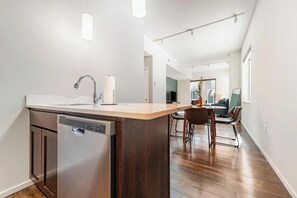 A modern kitchen with a dishwasher, a wooden island, and a dining area with chairs. - Landing | Beautiful 2BD, Yoga Studio, Gym (Omaha)